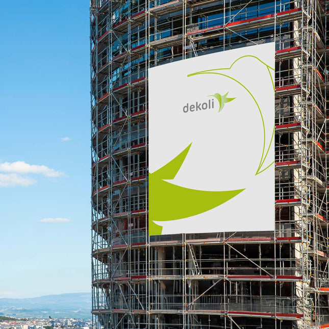 Großes Werbebanner von dekoli angebracht an einem Gerüst auf einer Baustelle mit blauem Himmel im Hintergrund, ideal für Großflächenwerbung und Markenpräsenz im urbanen Raum