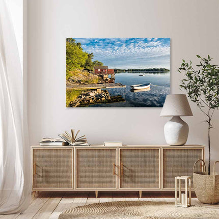 Leinwandbild mit der Schönheit skandinavischer Natur - idyllische Seenlandschaft mit traditionellem, rotem Holzhaus und weißem Boot am Steg. Die malerische Landschaft bringt die Idylle direkt in ihr Wohnzimmer und zaubert über dem Sideboard eine tolle Atmosphäre.