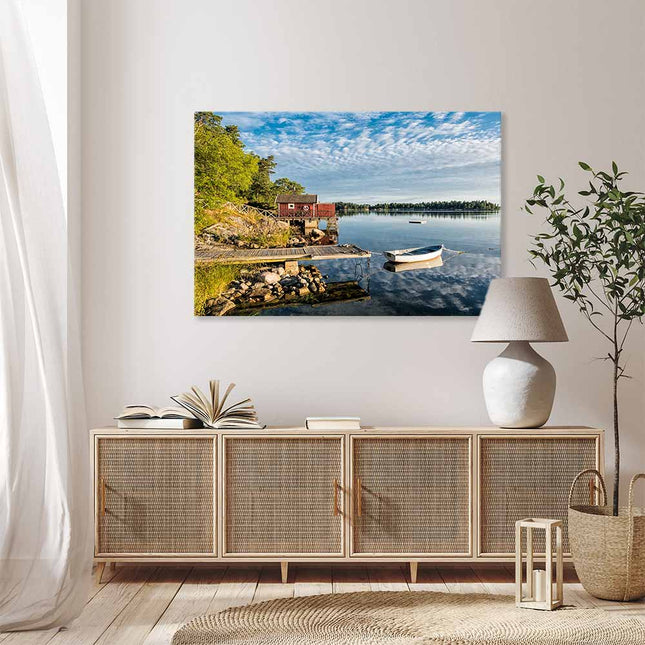Leinwandbild mit der Schönheit skandinavischer Natur - idyllische Seenlandschaft mit traditionellem, rotem Holzhaus und weißem Boot am Steg. Die malerische Landschaft bringt die Idylle direkt in ihr Wohnzimmer und zaubert über dem Sideboard eine tolle Atmosphäre.