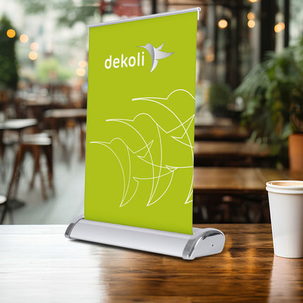 Ansicht RollUP Mini als Tischdisplay nutzbar als Menükarte oder Werbefläche. Als Größenvergleich neben einem Pappbecher